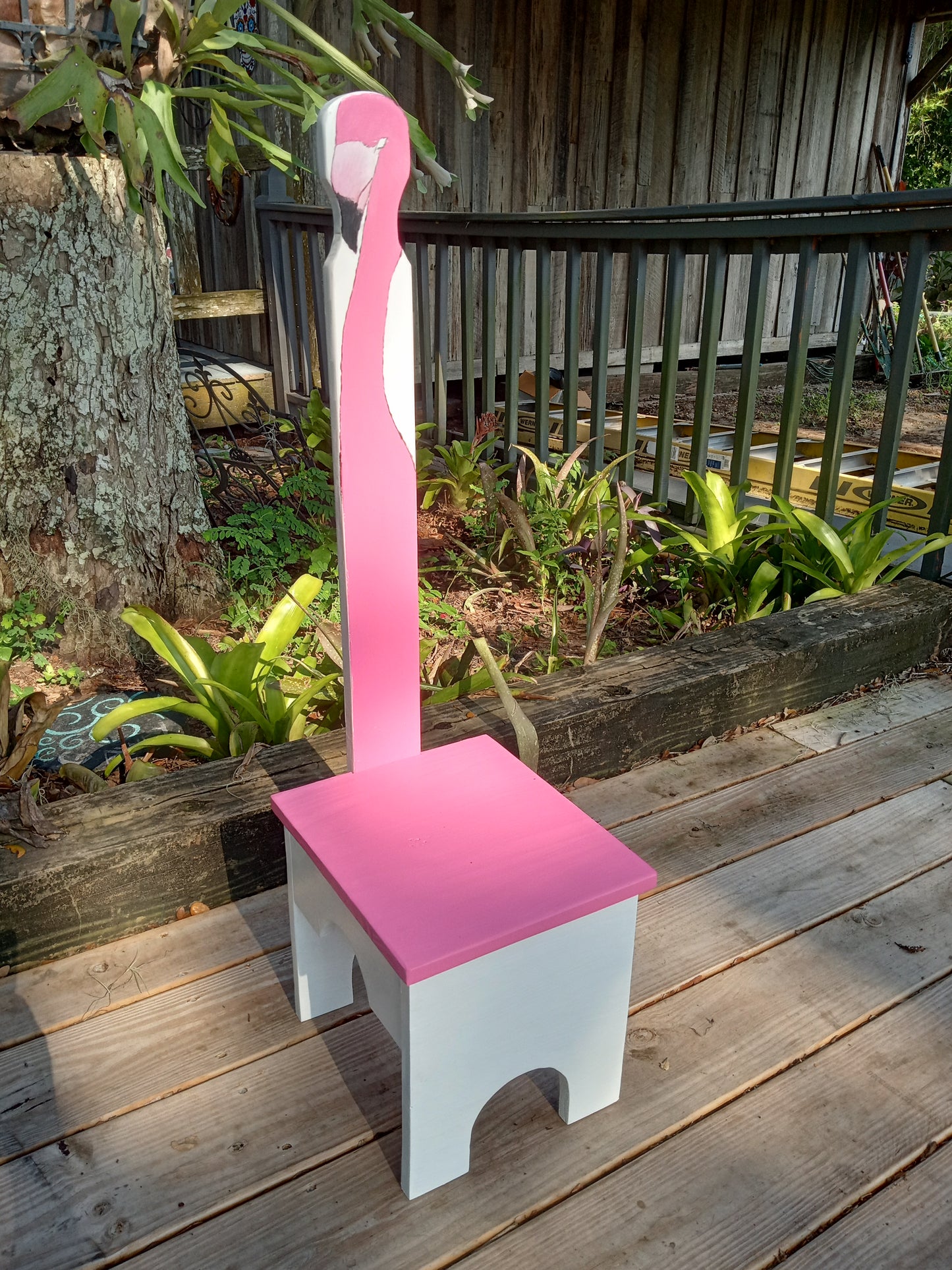 Pink and white Stable step stool on a wooden surface with plants in the background.