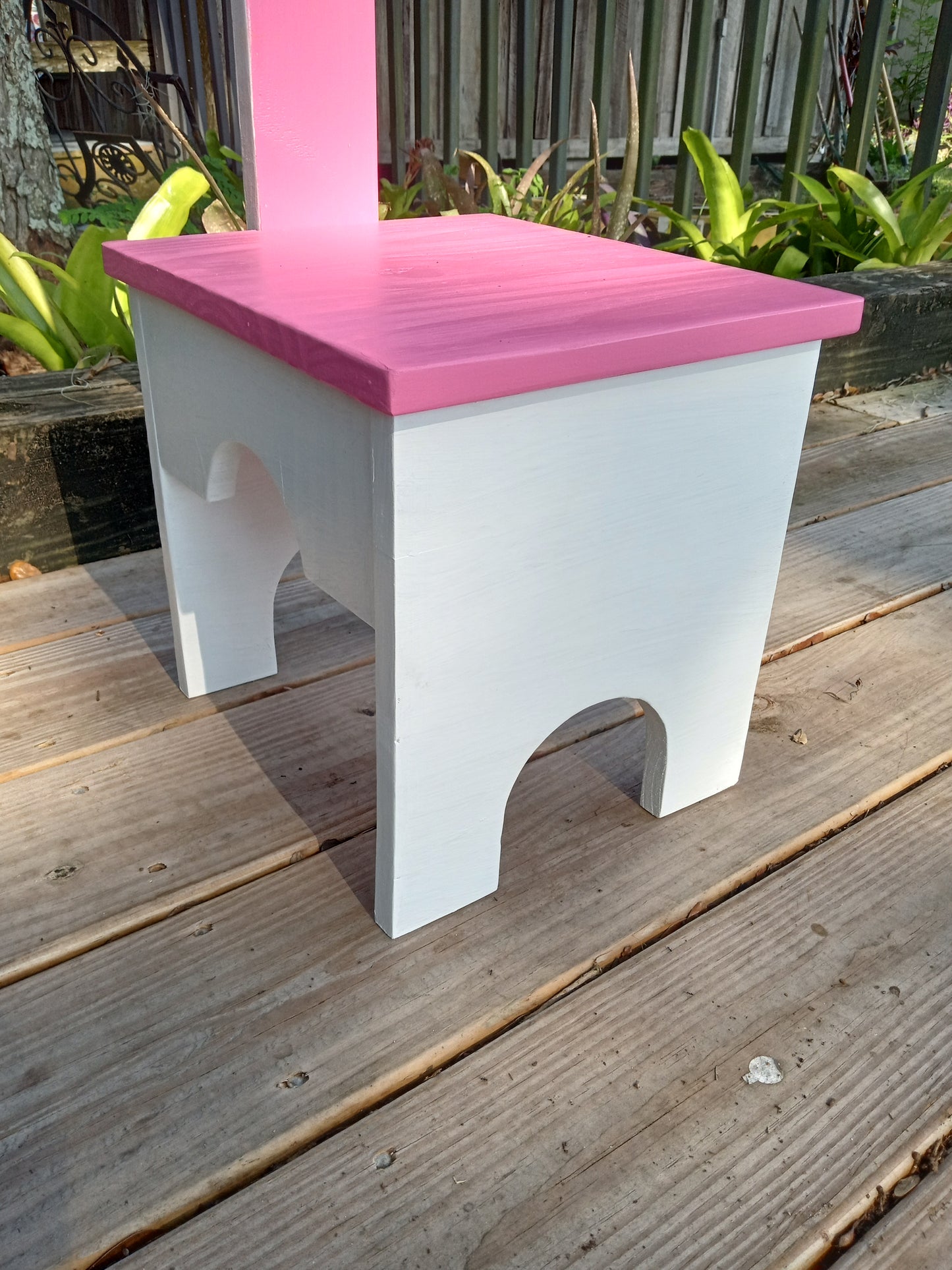 A closer look of one white and pink Stable step stool standing on a wooden deck.