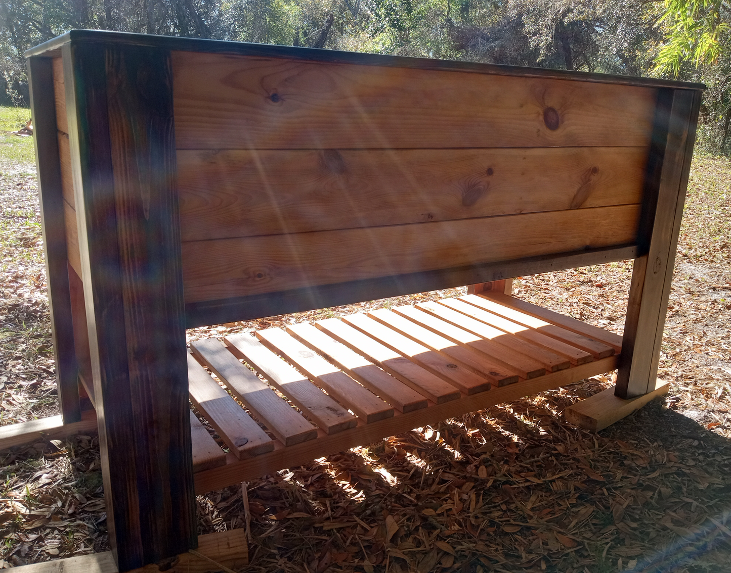 Handcrafted Raised Garden Box with slatted shelf, made from thick stained lumber, ideal for spring planting, highlighted by sunlight showcasing wood grain and durability.