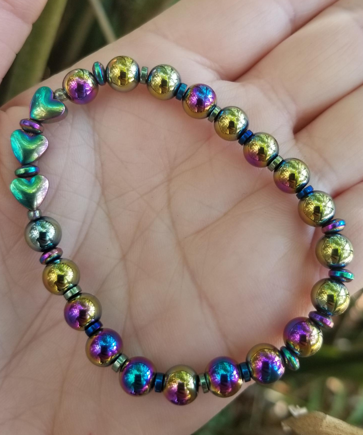 A multicolored beaded bracelet with round and rondelle beads, featuring metallic and rainbow hues, held in a person's hand.