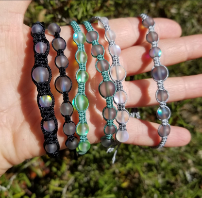 A hand holding four bracelets with multicolored beads and black or green cord.
