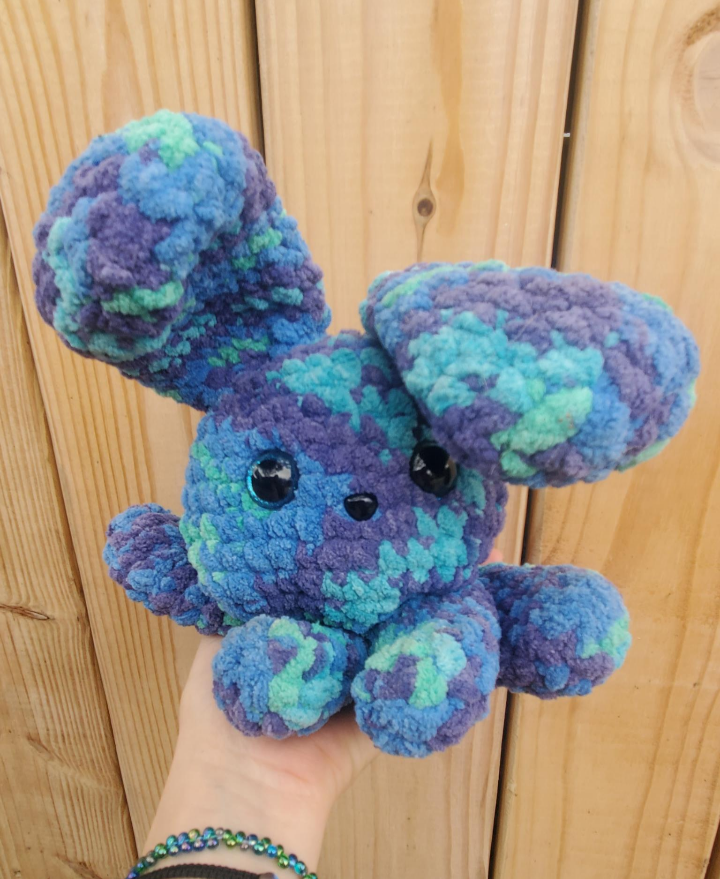 Crocheted blue and green creature held against a wooden background