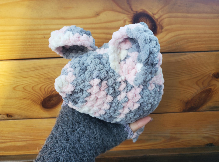 Crochet gray and pink mouse held against a wooden background