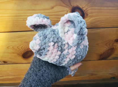 Crochet gray and pink mouse held against a wooden background