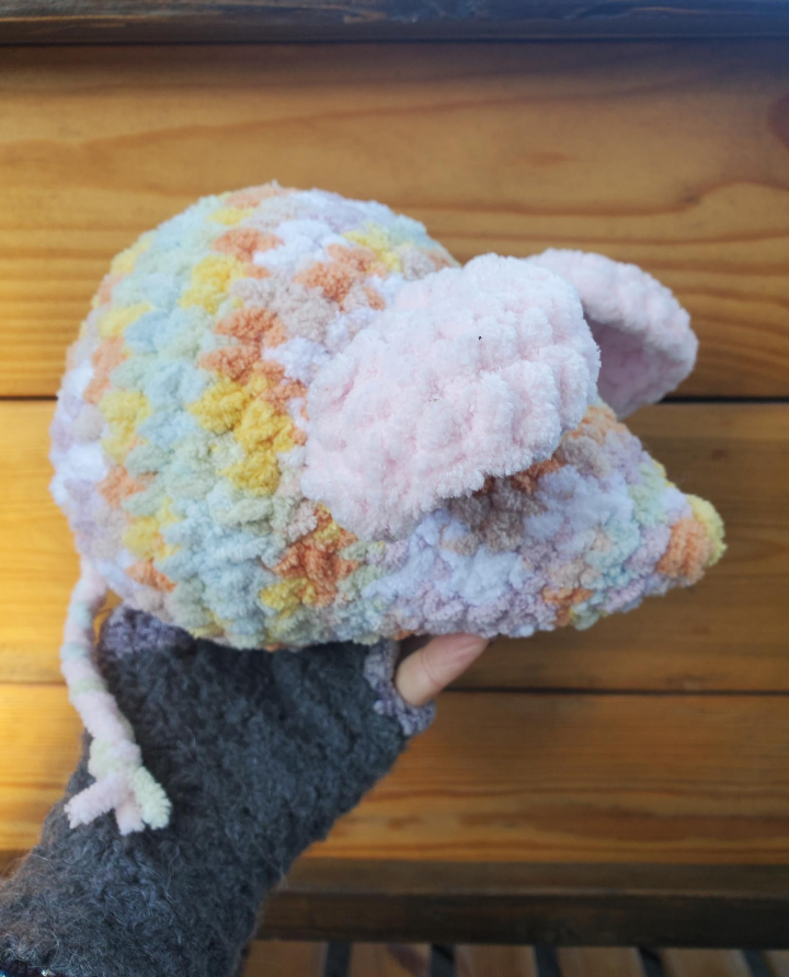 Colorful crochet mouse held by a hand on a wooden surface