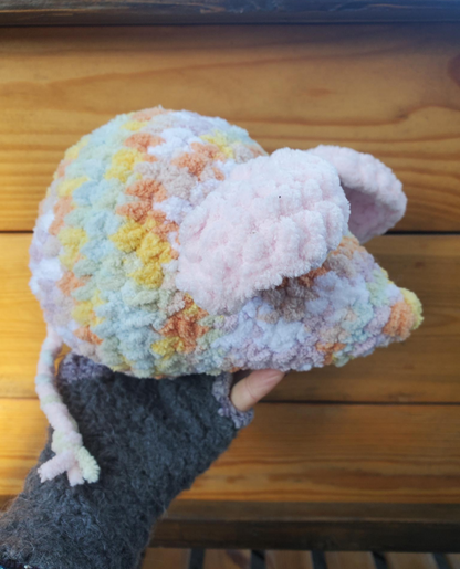 Colorful crochet mouse held by a hand on a wooden surface