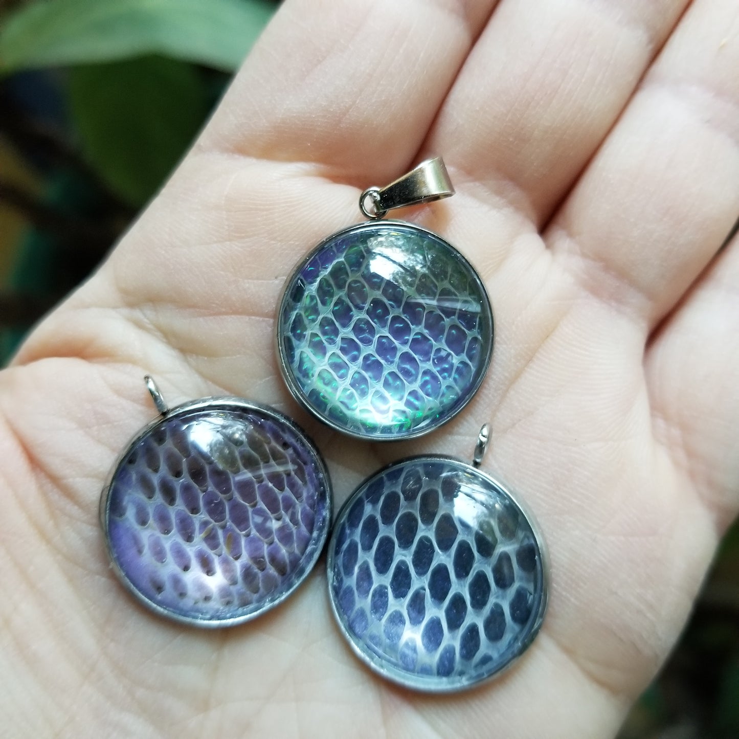 Three stainless steel pendants with snakeskin pattern held in a person's hand.