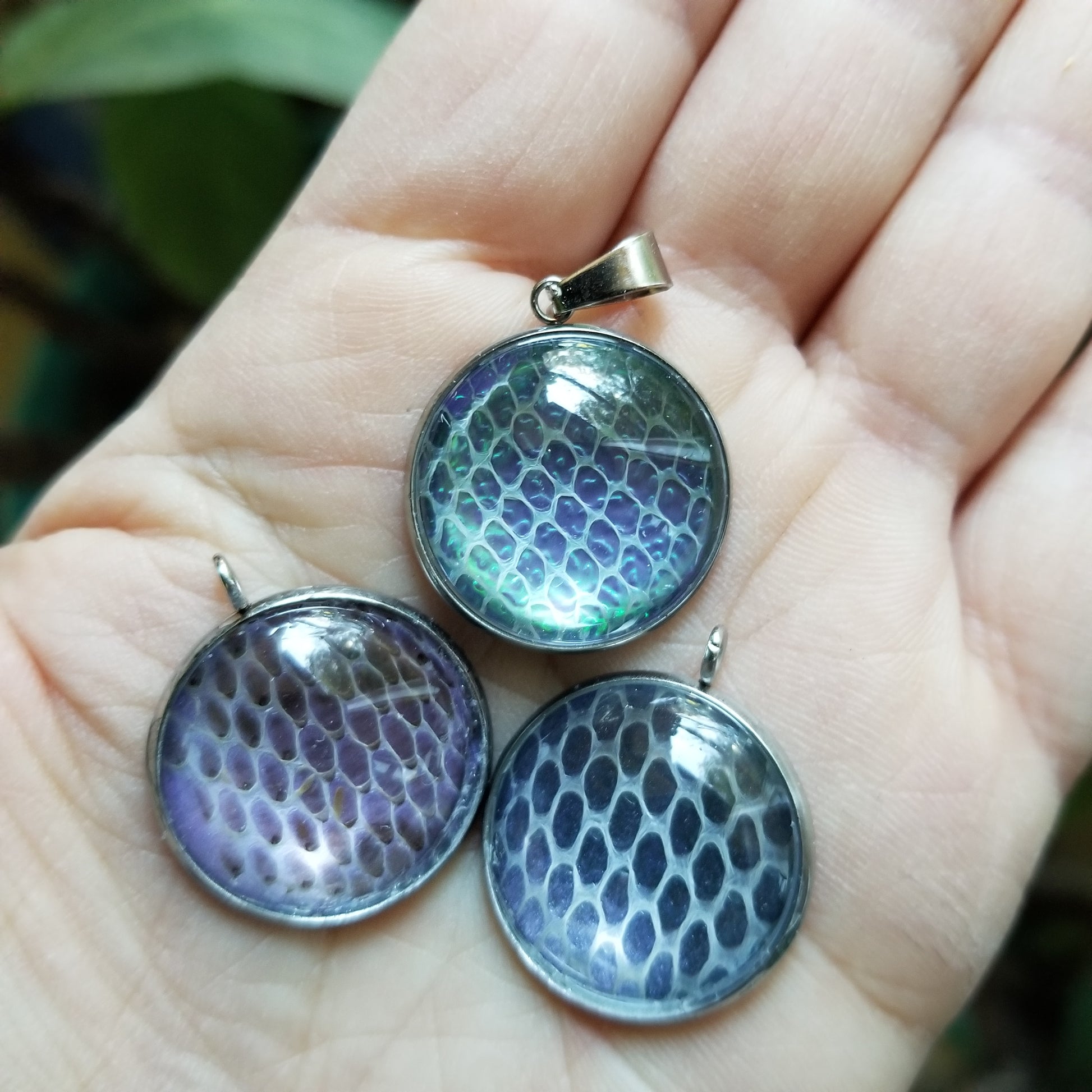 Three stainless steel pendants with snakeskin pattern held in a person's hand.