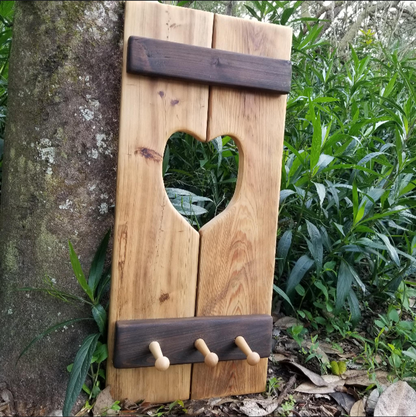 Cypress Wall Decor Coat Rack with heart cutout, three pegs, and rustic cross-planks, displayed outdoors, ideal for hanging coats and adding cozy charm.