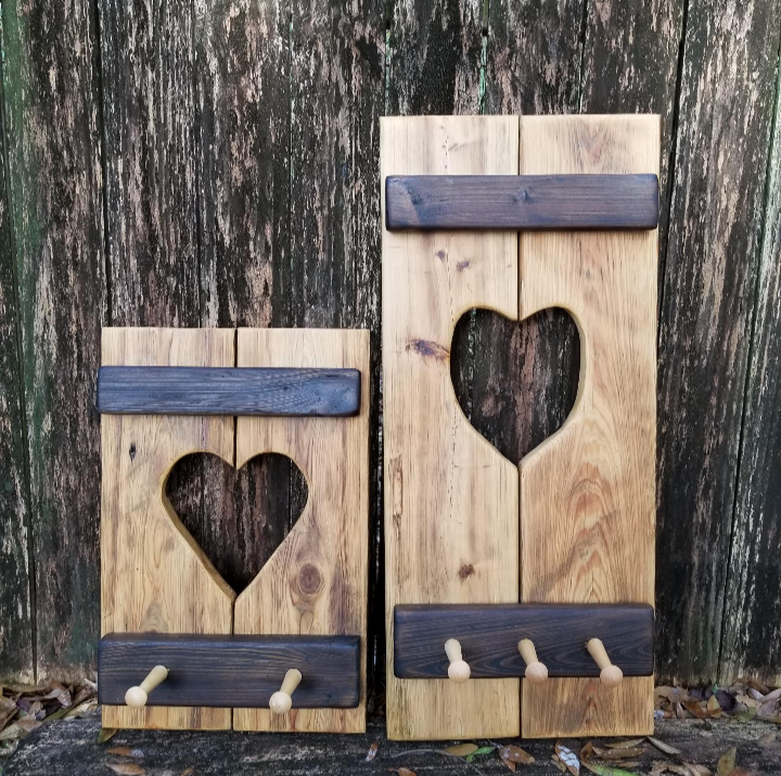 Two rustic Cypress Wall Decor Coat Racks with heart cutouts, featuring two and three pegs respectively, against a wooden backdrop.