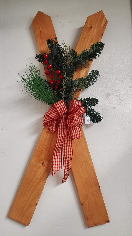 Decorative wooden ski with greenery and a red bow on a white background