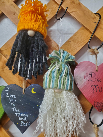 Two yarn-dressed gnomes hanging on a wooden surface with decorative hearts below.