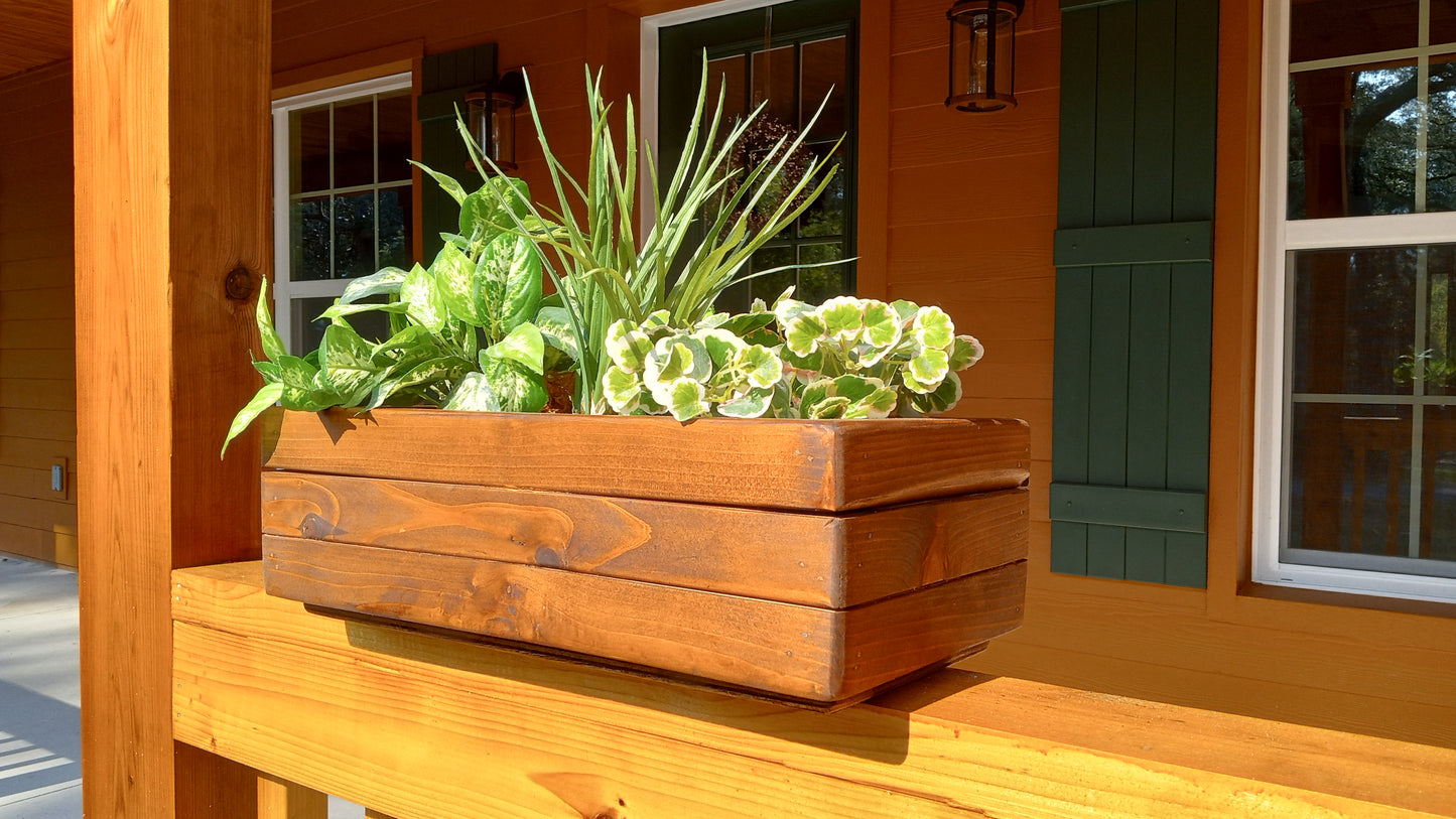 Large Cedar Planter Box on a porch railing, filled with varied green foliage, showcasing handcrafted cedar construction with mitered corners for strength.