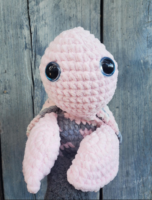 Pink crochet turtle with large eyes against a wooden background