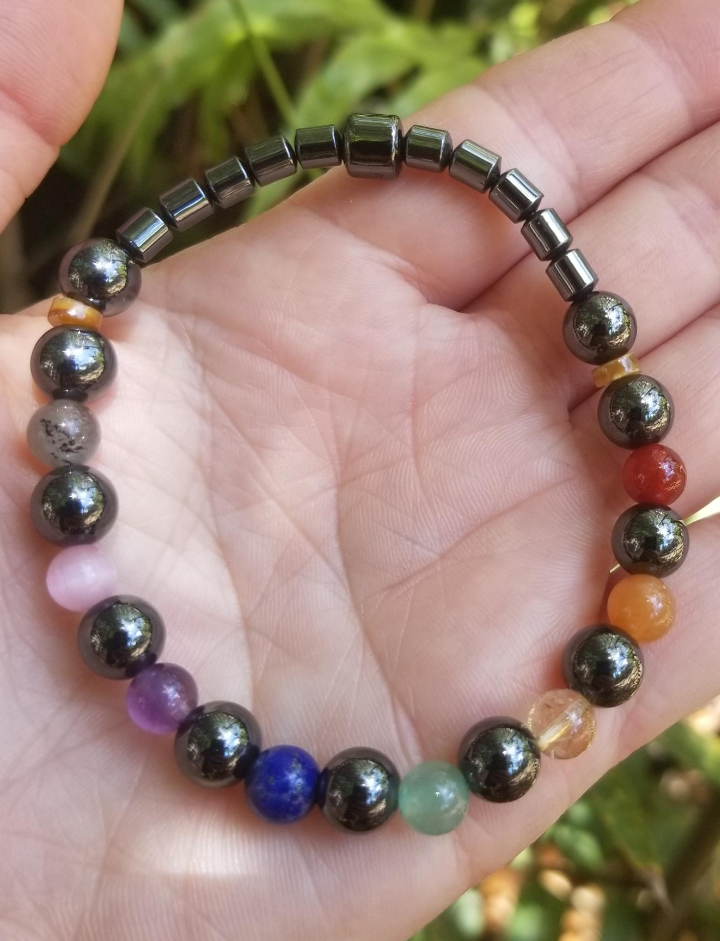 A hand holding a colorful beaded bracelet featuring a variety of stones and magnetic hematite beads on an elastic cord.