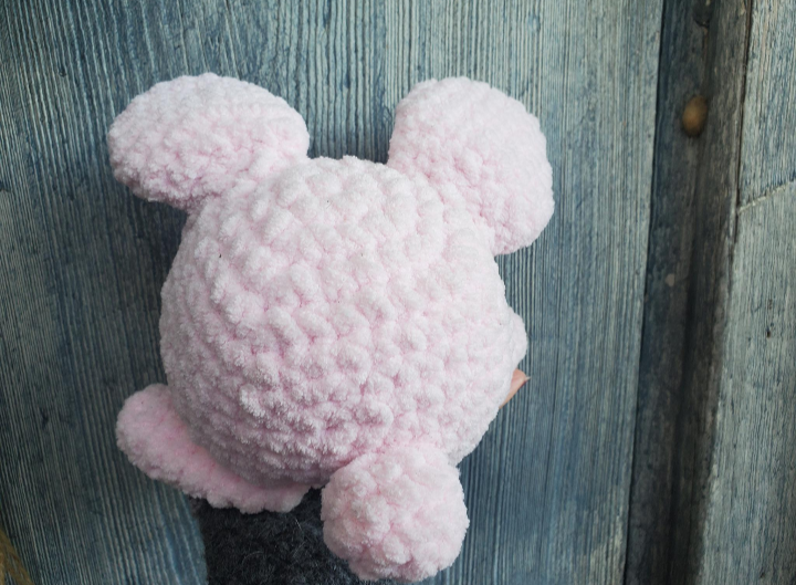 Pink crochet plush toy bunny back view on a wooden surface