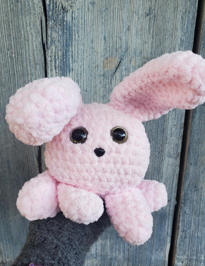 Pink crochet bunny toy against a wooden background