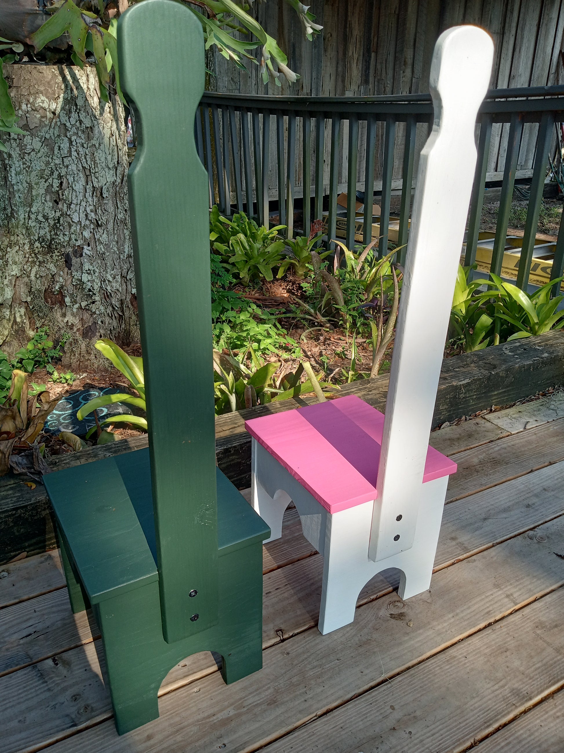 Two wooden step stools shown from behind, one white and one green, on a wooden surface with plants in the background.