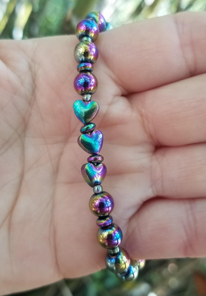 A multicolored beaded bracelet with round and rondelle beads, featuring metallic and rainbow hues, held in a person's hand.