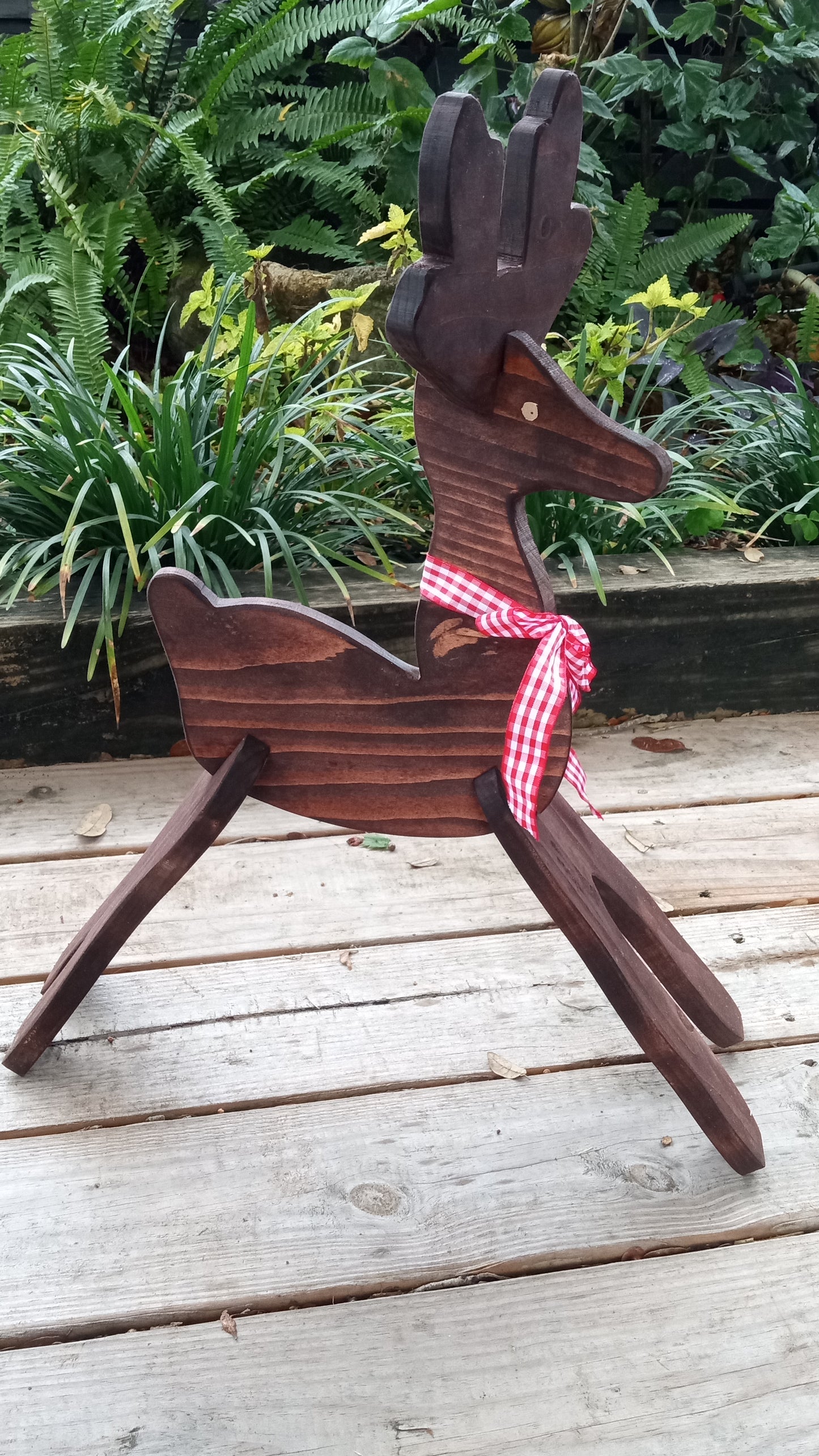 Wooden reindeer with a red and white checkered ribbon on a wooden floor with plants in the background