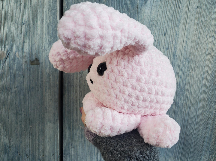 Pink crochet bunny held by a person against a wooden background