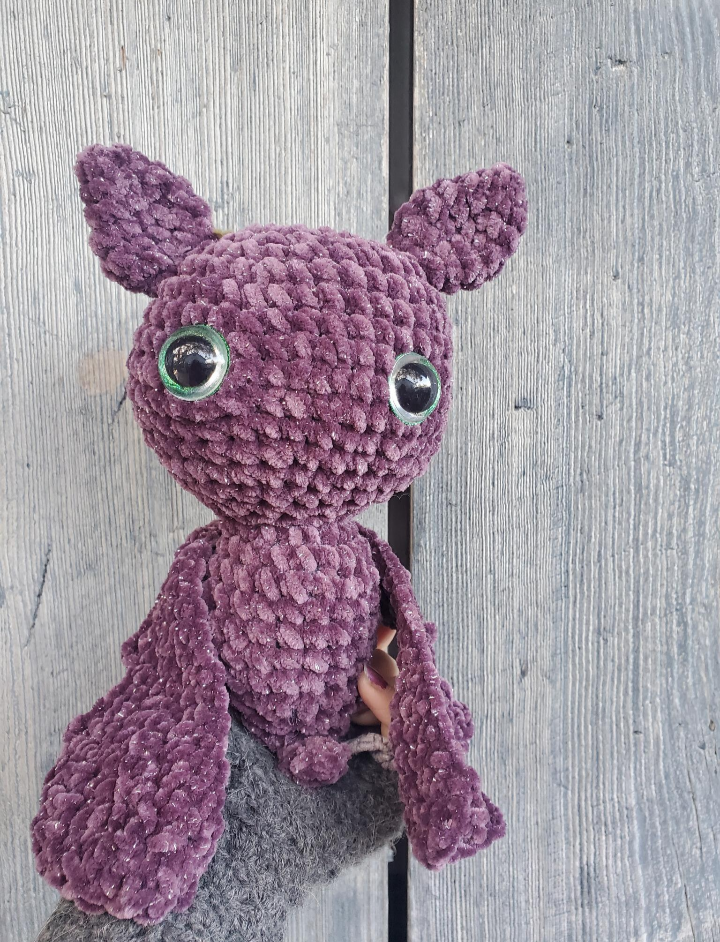Purple crochet bat held by a person against a wooden background