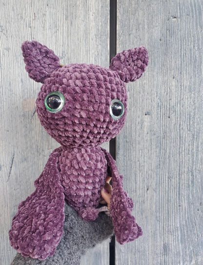 Purple crochet bat held by a person against a wooden background