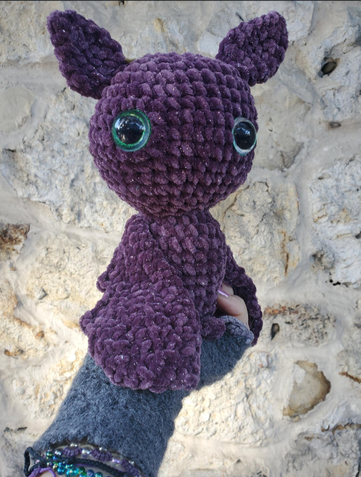 Purple crochet bat toy held by a person against a stone background