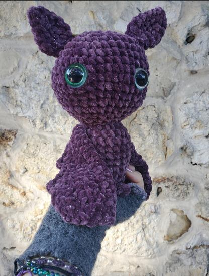Purple crochet bat toy held by a person against a stone background